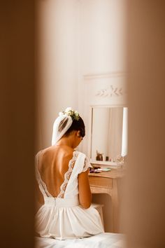 a woman in a white dress sitting on a bed looking at herself in the mirror