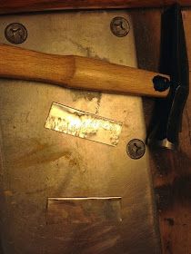 an old metal box with a wooden handle and hammer on it's side, in front of a wood paneled wall