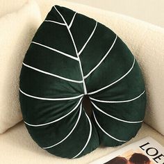 a green leaf shaped pillow sitting on top of a white couch next to a magazine