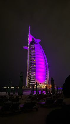 the burj building is lit up in purple light at night, and people are standing near it