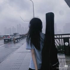 a woman walking down the street with an acoustic guitar case in her hand and rain falling on her head