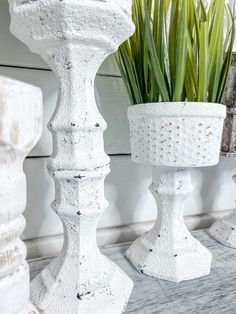 two white vases sitting on top of a wooden table next to a potted plant