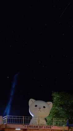 a large white cat statue sitting on top of a wooden bridge under a sky filled with stars