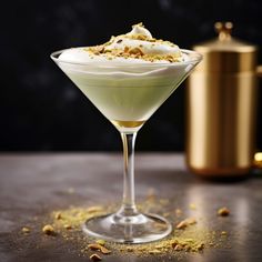 a martini glass filled with green liquid and topped with whipped cream, nuts and crumbles