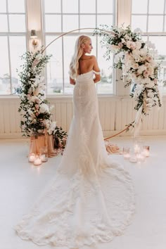 a woman in a wedding dress standing next to a floral arch with candles and flowers