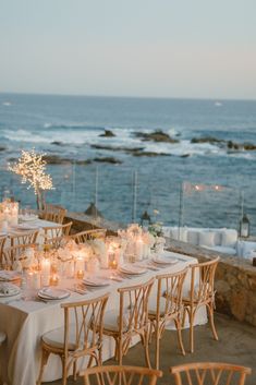 a long table with candles and flowers on it near the ocean in front of some rocks