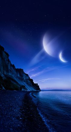 two crescents are seen in the night sky over an ocean and rocky cliff face