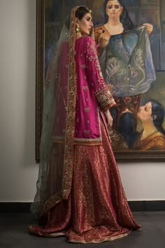 a woman standing in front of a painting wearing a pink and gold lehenga