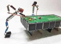 two robot arms are holding up a green table top with electronic components attached to it