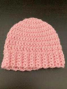 a pink crocheted beanie sitting on top of a black table next to a pair of scissors