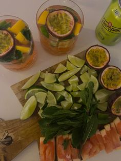 a cutting board topped with sliced up fruit and veggies next to two drinks