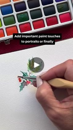 a person is drawing with watercolors on paper and using a pencil to draw holly leaves