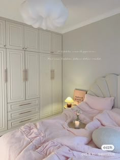 a white bed with pink sheets and pillows in a room next to some cupboards