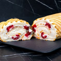 a roll with cream cheese and strawberries on it sitting on a black plate next to a marble counter top