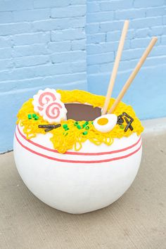 a bowl with chopsticks in it sitting on the ground next to a blue wall