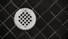 a black and white tile with a metal grate in the center that has a diamond design on it