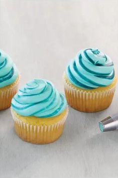 three cupcakes with blue frosting next to an electric pen on a white surface