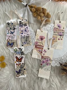 three tags with butterflies on them are laying on a white furnishing next to two teddy bears