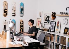 a man sitting at a desk in front of a laptop computer with lots of skateboards on the wall behind him