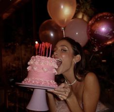 a woman holding a pink cake with candles in her mouth and blowing out the candles on it