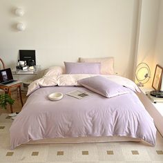 a bedroom with a bed covered in lavender colored sheets and pillows next to a desk