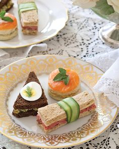 a plate with sandwiches and cucumbers on it sitting on a lace tablecloth