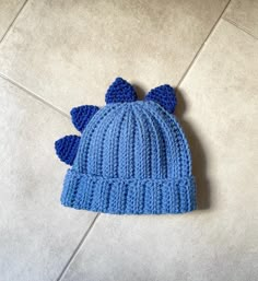 a blue knitted hat with bows on the side laying on a tile floor next to a tiled floor