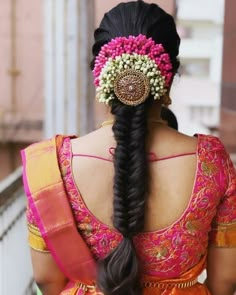 a woman with long black hair wearing an orange and pink saree, braided into a ponytail