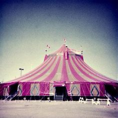 a pink and white circus tent sitting on top of a field