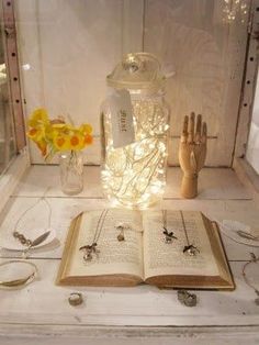 an open book sitting on top of a white table next to jewelry and flowers in a vase