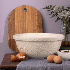 a white bowl sitting on top of a table next to eggs and a cutting board