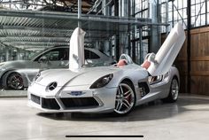 a silver sports car parked in front of a building with its doors open and the hood up