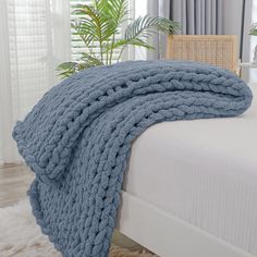 a bed with a blue blanket on top of it next to a chair and potted plant