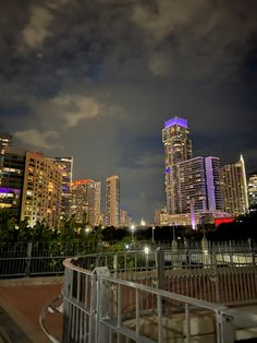 the city skyline is lit up at night with clouds in the sky and buildings on either side