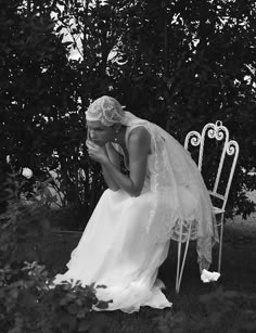 black and white photograph of a bride sitting on a chair in front of a bush