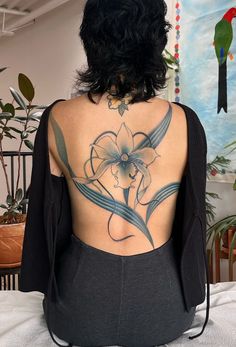 a woman sitting on top of a bed with a flower tattoo on her upper back