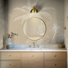 a bathroom vanity with a round mirror and palm tree wallpaper on the wall behind it