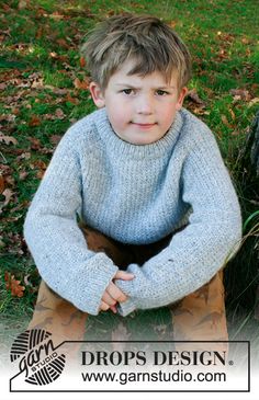 a young boy sitting on the ground wearing a sweater