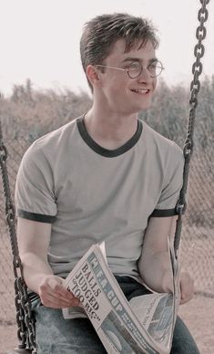 a man sitting on a swing holding a newspaper and looking at the camera with glasses