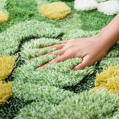 a person's hand on a rug with green and yellow flowers