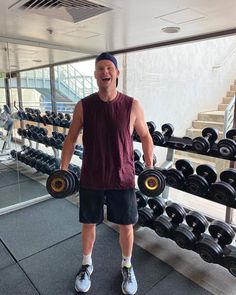 a man holding two dumbs in front of a rack of dumbs at the gym