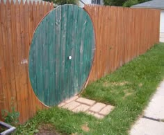 a wooden fence with a green door in the center and brick walkway leading to it