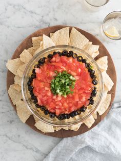 a bowl filled with salsa and tortilla chips on top of a wooden plate