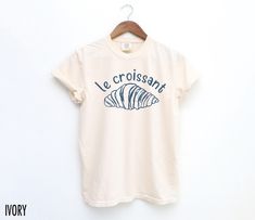 "Le Croissant" Graphic Tee - Serve up Parisian vibes with a side of chic in this cute, French café-inspired essential! We use professional quality DGT printing on all our apparel. Direct-to-garment, or DTG, is a high quality printing method that sprays ink directly onto the garment so there is no peeling or cracking. This fabulous graphic will be printed on a Comfort Colors Unisex T-Shirt. Please refer to the size charts in the images for the best fit.  Estimated Production Time: 1-5 days Estima Girl Travel Aesthetic, French Girl Aesthetic, Parisian Vibes, Aesthetic Retro, Paris T Shirt, French Cafe, Retro Graphic Tees, Cafe Style, Third Birthday