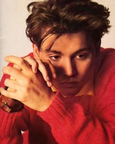 a man in a red sweater is posing with his hands on his face and looking at the camera