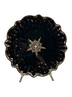 a black and gold plate with an ornate star on it's center, sitting on a metal stand