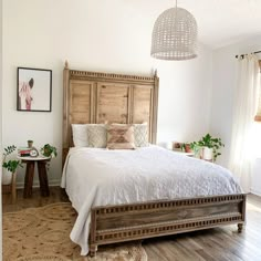 a bedroom with white bedding and wooden headboard, potted plants on the side table