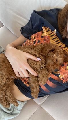 a woman laying on a couch holding a brown dog with her face close to the camera