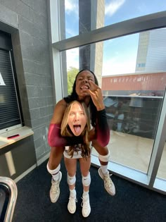 two women are posing for the camera in front of a large window with their mouths open