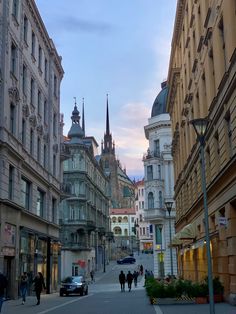 people are walking down the street in an old european city at sunset or sunrise time